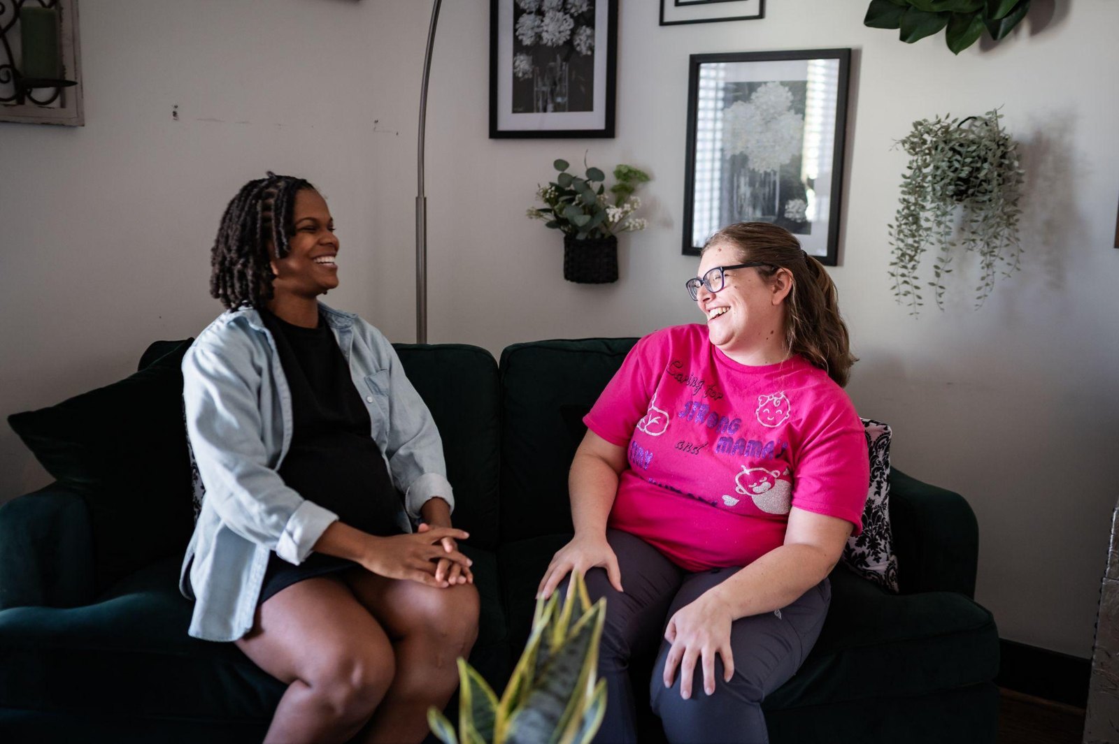Two women sitting on a couch, one pregnant and one acting as a doula, talking and smiling