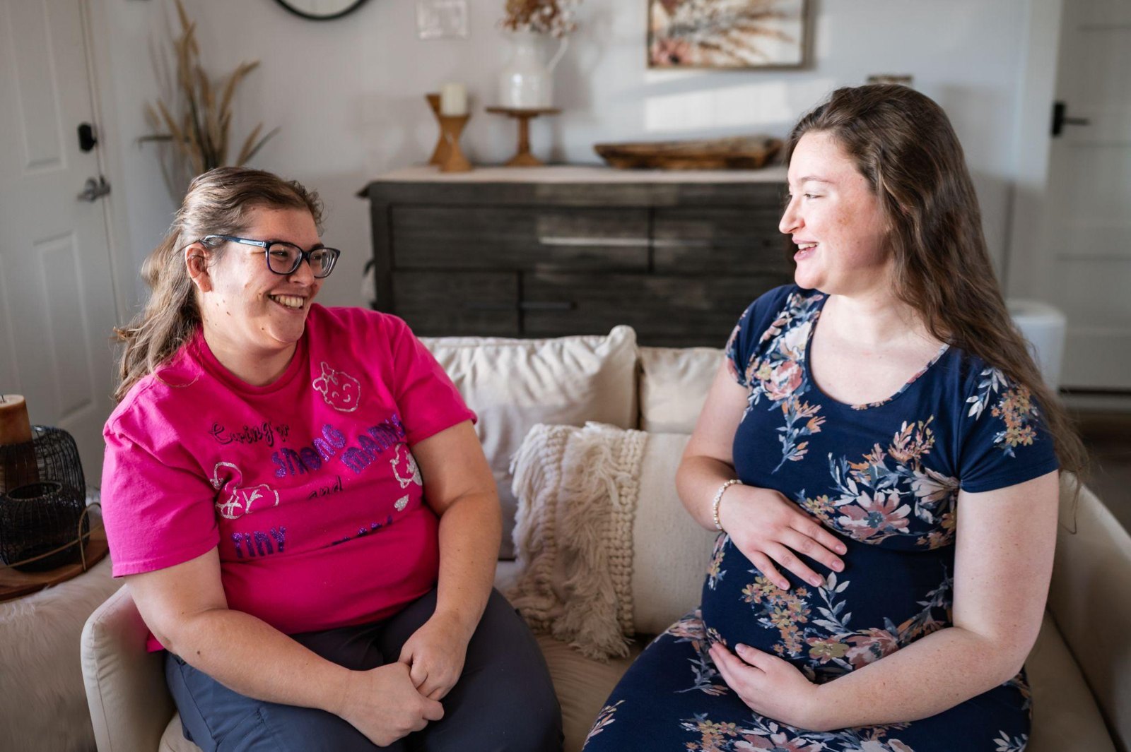 Two women sitting on a couch, one pregnant and one acting as a doula, talking and smiling