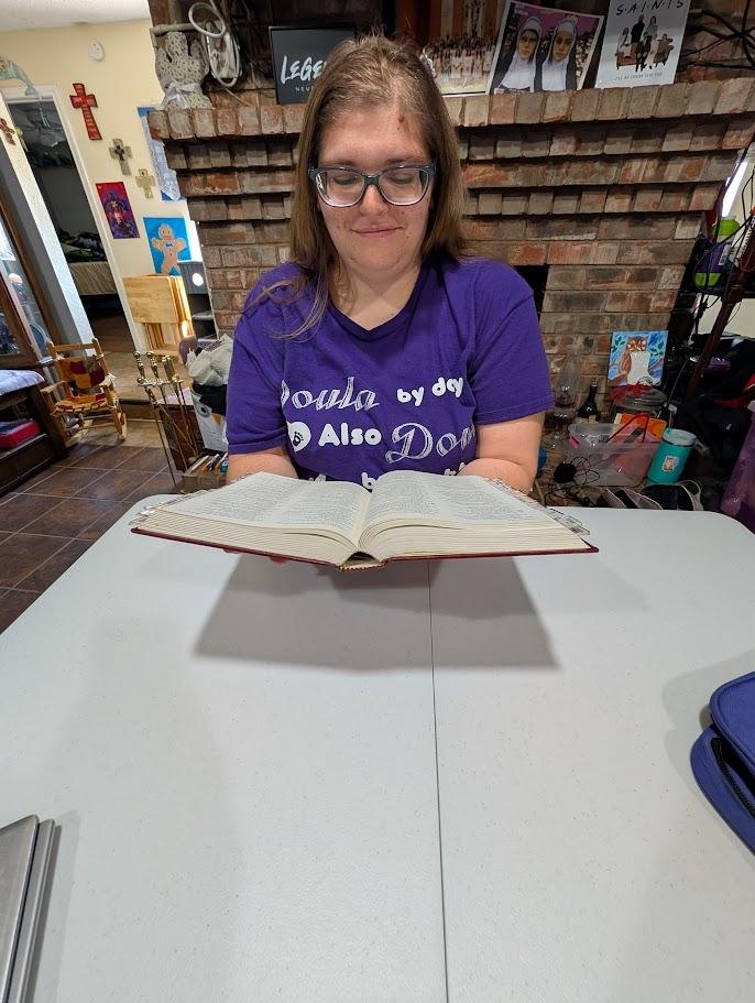 A woman wearing a purple shirt reading a book at a table